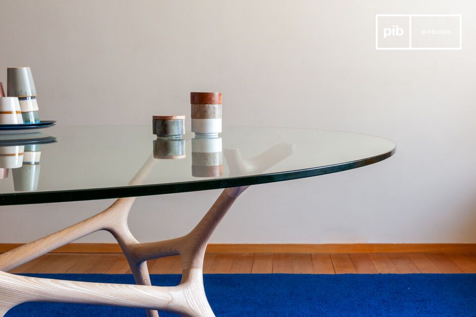 Son plateau en verre trempé repose sur un piètement sculpté qui rappelle la structure des